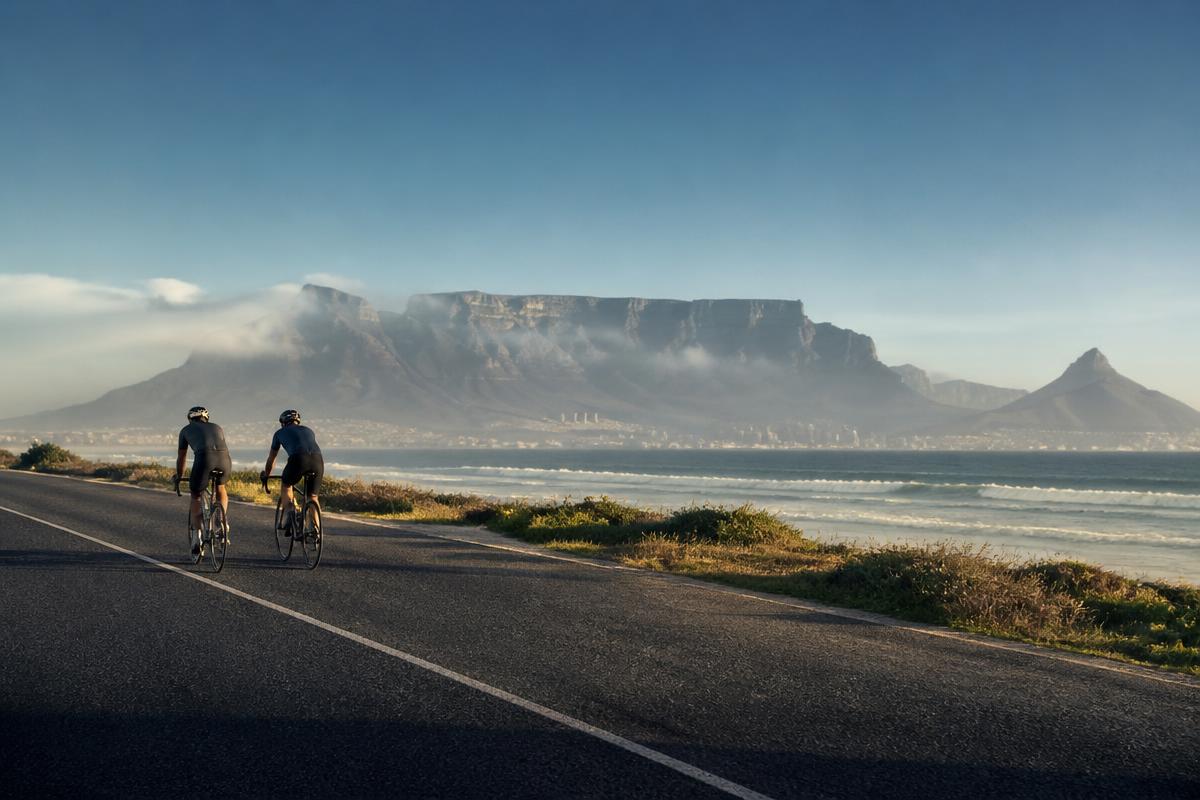 Two cyclists riding the Big Bay coastal road with Table Mountain beyond